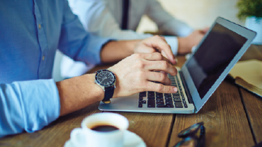 Person typing on laptop next to cup of coffee